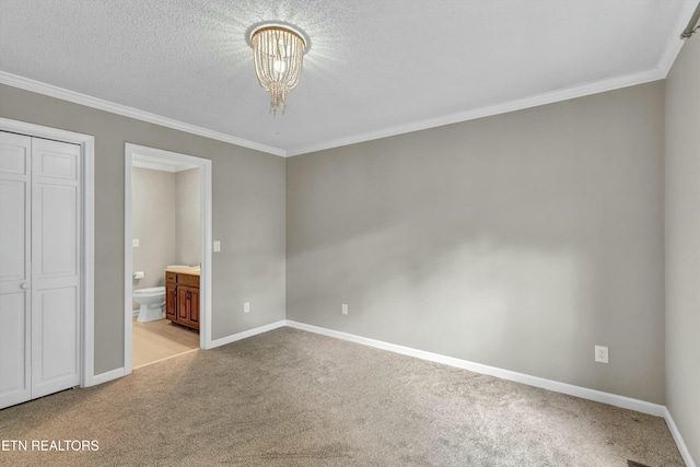 unfurnished bedroom featuring carpet floors, ornamental molding, connected bathroom, a chandelier, and baseboards