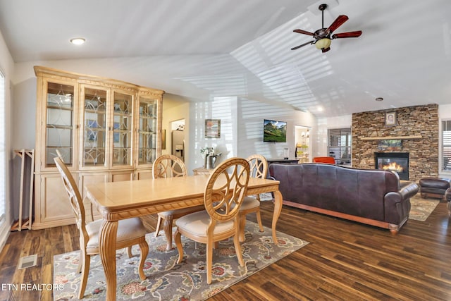 dining space with visible vents, dark wood finished floors, lofted ceiling, a stone fireplace, and a ceiling fan