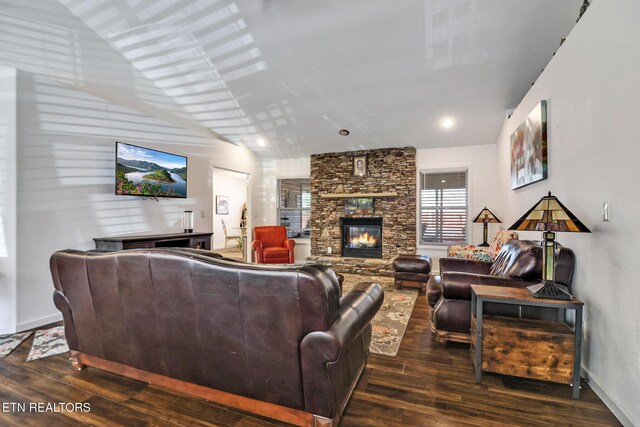 living room featuring baseboards, a stone fireplace, dark wood finished floors, and vaulted ceiling