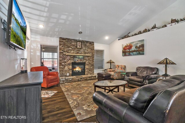 living room featuring dark wood finished floors, vaulted ceiling, and a stone fireplace