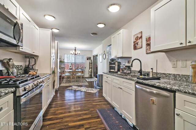 kitchen featuring dark stone countertops, stainless steel appliances, dark wood-type flooring, white cabinetry, and a notable chandelier