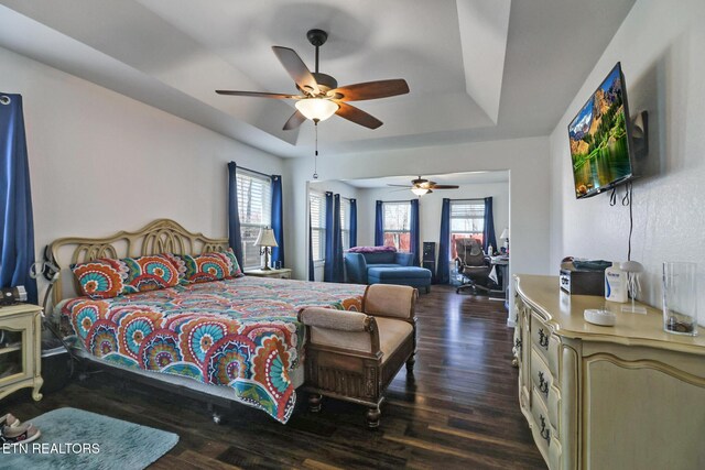 bedroom featuring a raised ceiling, a ceiling fan, and dark wood-style flooring