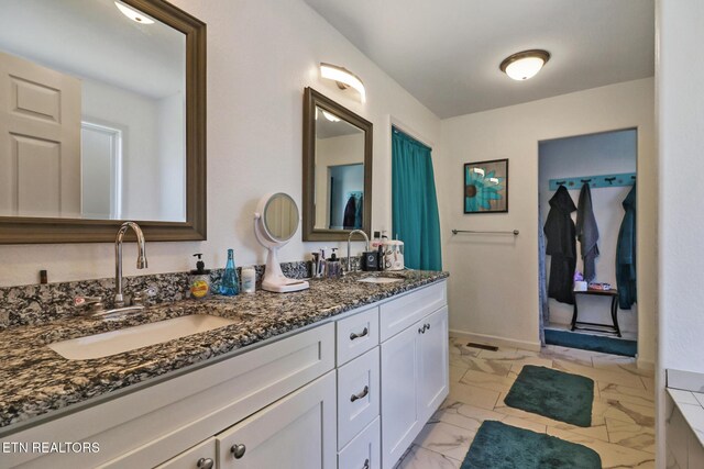 full bath with double vanity, marble finish floor, baseboards, and a sink