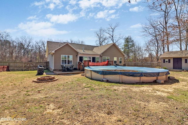 back of property with a fenced backyard, a yard, a fire pit, a wooden deck, and a fenced in pool