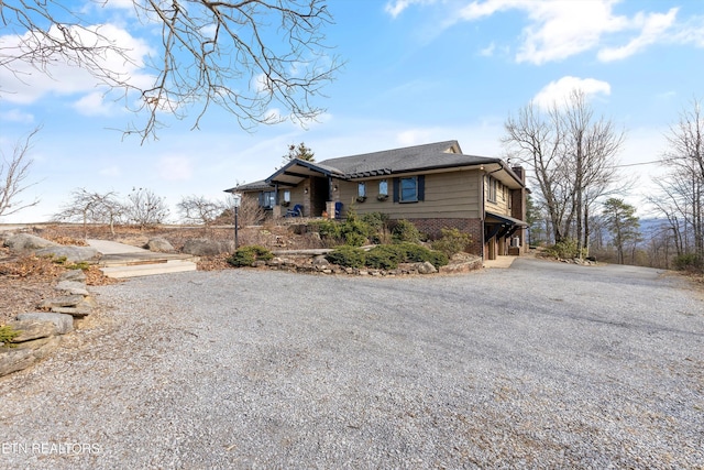 view of front of property featuring gravel driveway, brick siding, and a chimney