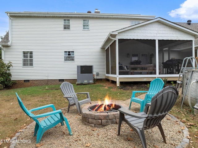 rear view of property featuring a sunroom, an outdoor fire pit, crawl space, and a lawn