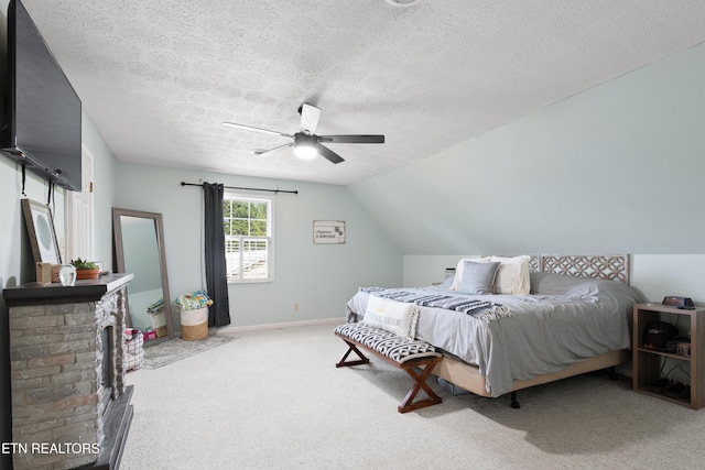 carpeted bedroom featuring baseboards, a ceiling fan, vaulted ceiling, a textured ceiling, and a fireplace