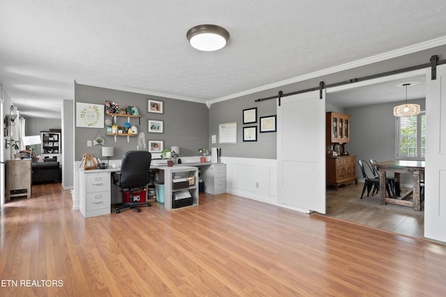 home office with light wood finished floors, a barn door, a textured ceiling, and a wainscoted wall