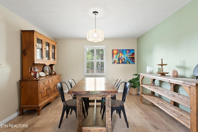 dining area with baseboards, a textured ceiling, and light wood-style floors