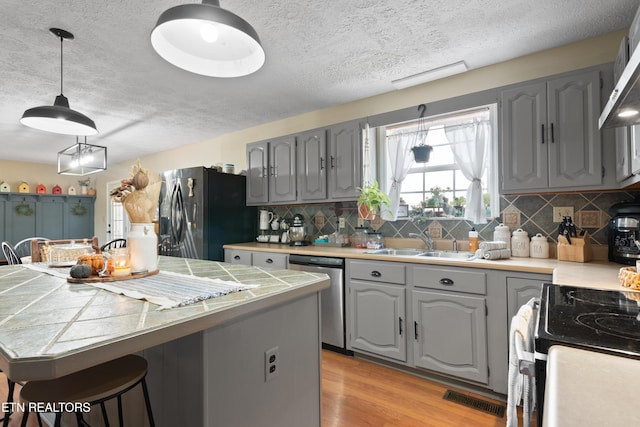 kitchen with gray cabinets, stainless steel appliances, light wood-type flooring, wall chimney range hood, and a sink