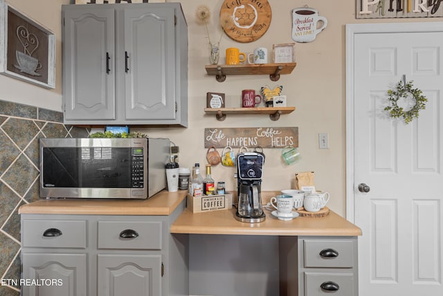 kitchen with light countertops, stainless steel microwave, open shelves, and decorative backsplash