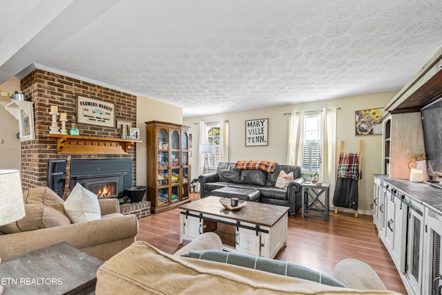 living room featuring a brick fireplace, a textured ceiling, baseboards, and wood finished floors