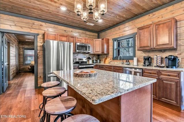 kitchen featuring light wood finished floors, stainless steel appliances, a sink, wooden walls, and wooden ceiling