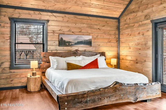 bedroom featuring lofted ceiling, multiple windows, wooden walls, and wood finished floors