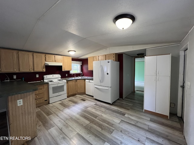 kitchen with white appliances, light wood-style floors, dark countertops, under cabinet range hood, and a sink