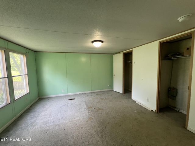 unfurnished bedroom with carpet floors, a textured ceiling, and multiple closets