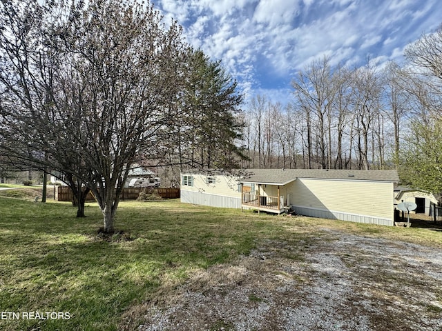 view of yard with gravel driveway, a deck, and fence