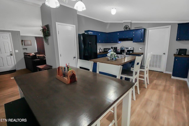 kitchen featuring visible vents, dark countertops, freestanding refrigerator, under cabinet range hood, and blue cabinetry