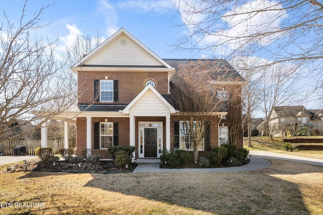 view of front of property featuring a porch, brick siding, fence, and a front lawn