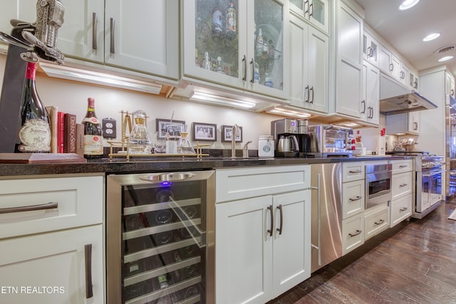 kitchen with beverage cooler, appliances with stainless steel finishes, dark countertops, dark wood finished floors, and glass insert cabinets