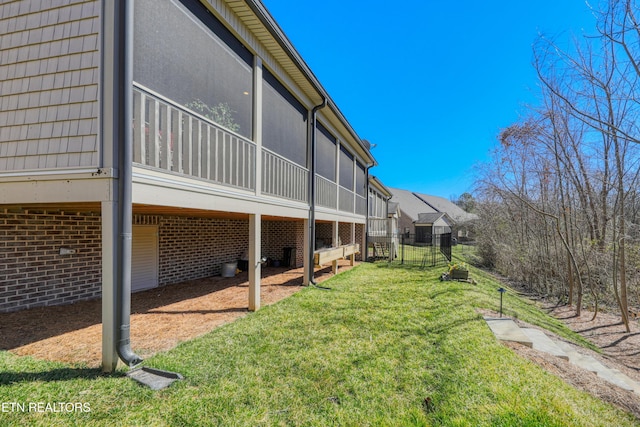 view of side of property featuring brick siding, a lawn, and a sunroom