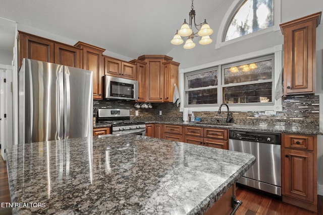 kitchen featuring dark wood-type flooring, a sink, appliances with stainless steel finishes, backsplash, and brown cabinetry