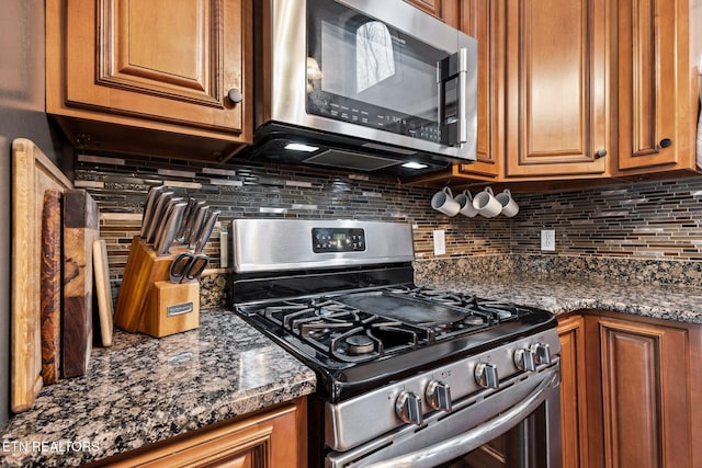 kitchen featuring brown cabinetry, dark stone countertops, stainless steel appliances, and decorative backsplash