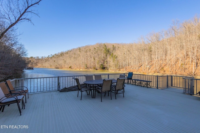 wooden terrace with outdoor dining space, a water view, and a wooded view