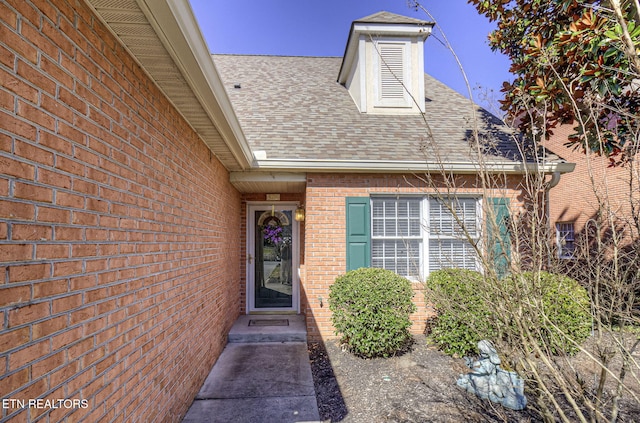 view of exterior entry with brick siding and roof with shingles