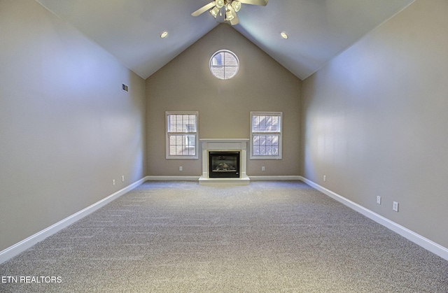 unfurnished living room with baseboards, visible vents, a glass covered fireplace, carpet floors, and high vaulted ceiling