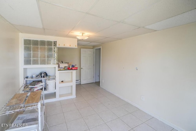 spare room with light tile patterned flooring, a paneled ceiling, and baseboards