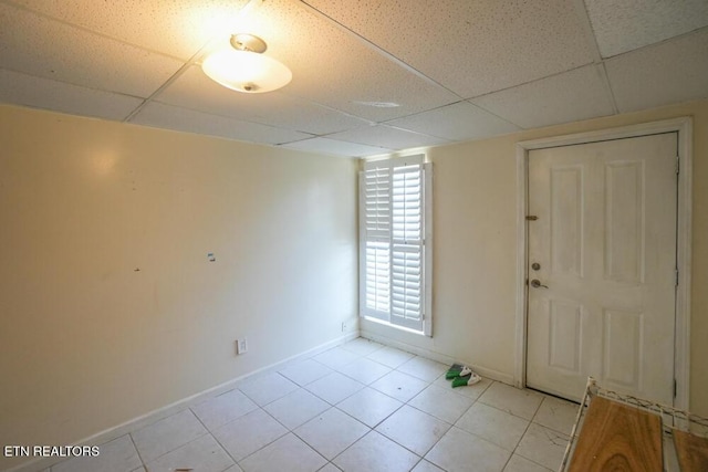 interior space with baseboards, a drop ceiling, and light tile patterned flooring