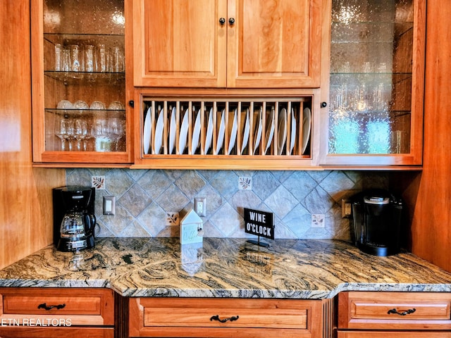 kitchen featuring backsplash, glass insert cabinets, and light stone countertops