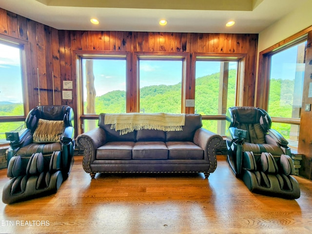 living room with recessed lighting, wood walls, a tray ceiling, and wood finished floors