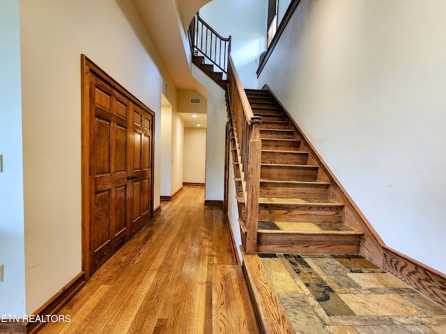 stairs featuring baseboards, a high ceiling, visible vents, and wood finished floors