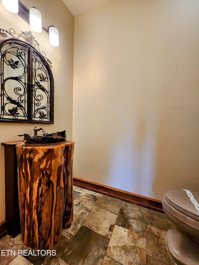 bathroom featuring stone finish flooring, toilet, vanity, and baseboards