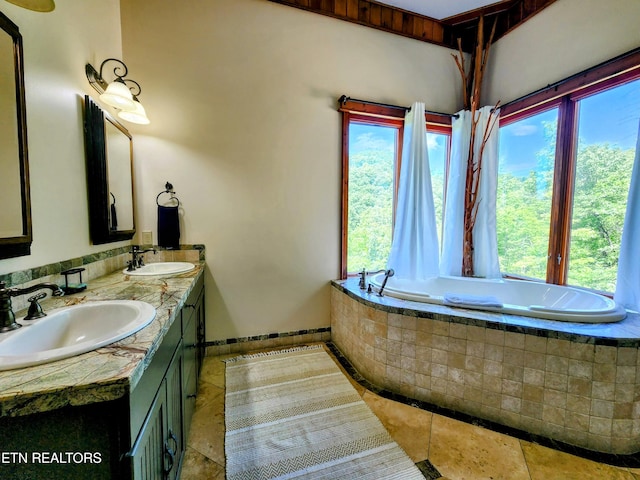 full bath with a relaxing tiled tub, a sink, baseboards, and double vanity