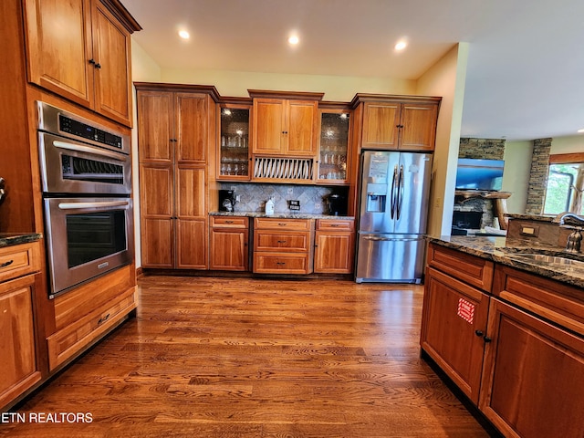 kitchen with dark wood-style flooring, tasteful backsplash, appliances with stainless steel finishes, glass insert cabinets, and a sink