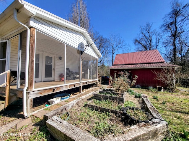 view of side of property featuring a sunroom, metal roof, and a garden