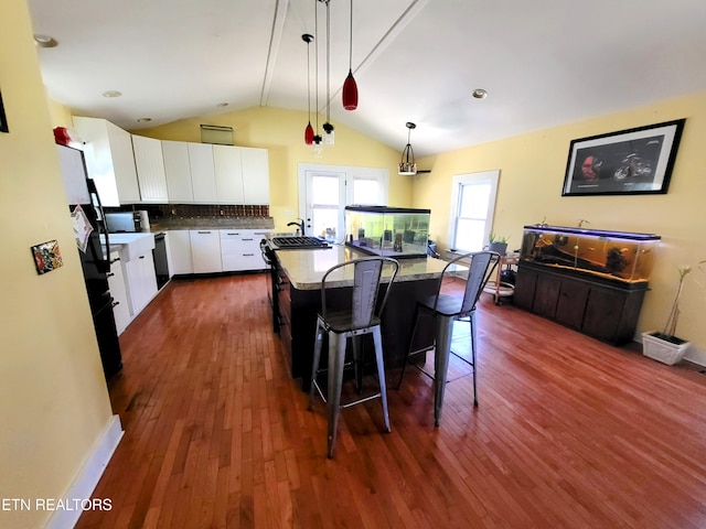 kitchen featuring tasteful backsplash, white cabinets, dark wood finished floors, a center island, and a kitchen bar