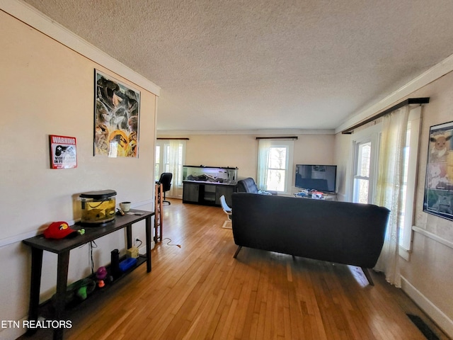 living area with crown molding, a textured ceiling, and hardwood / wood-style floors