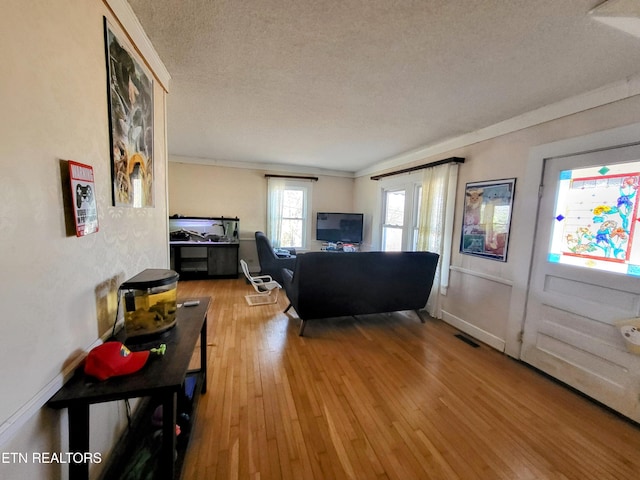 living room with visible vents, ornamental molding, a textured ceiling, baseboards, and hardwood / wood-style flooring