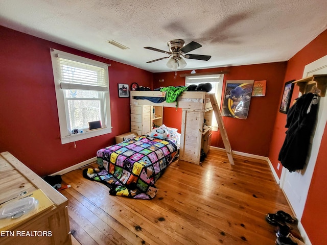 bedroom featuring wood-type flooring, visible vents, a textured ceiling, and baseboards