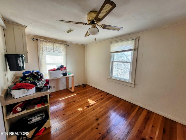 interior space with a ceiling fan, wood-type flooring, visible vents, and multiple windows