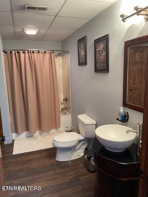 bathroom featuring toilet, a paneled ceiling, wood finished floors, visible vents, and shower / bath combo