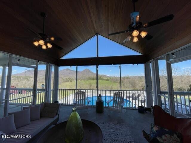 sunroom with lofted ceiling, wood ceiling, a mountain view, and ceiling fan