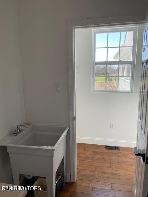 interior space with a sink, wood finished floors, visible vents, and baseboards