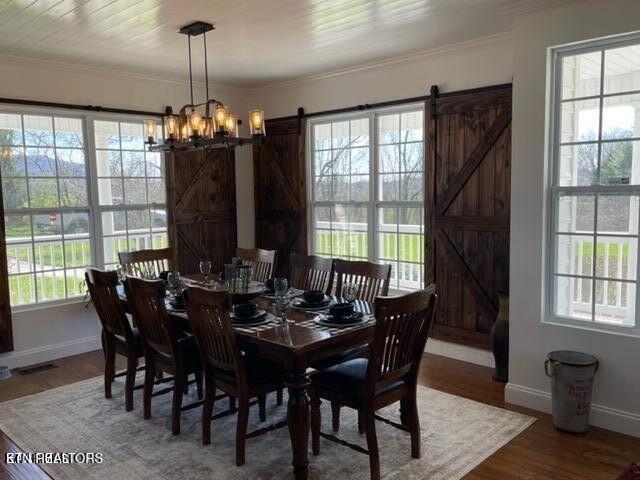 dining area featuring a barn door, wood finished floors, and crown molding