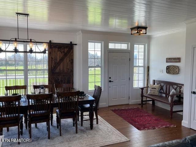 dining area featuring ornamental molding, a barn door, baseboards, and wood finished floors