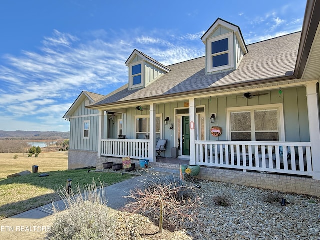 cape cod house with a porch, board and batten siding, a shingled roof, and a front yard